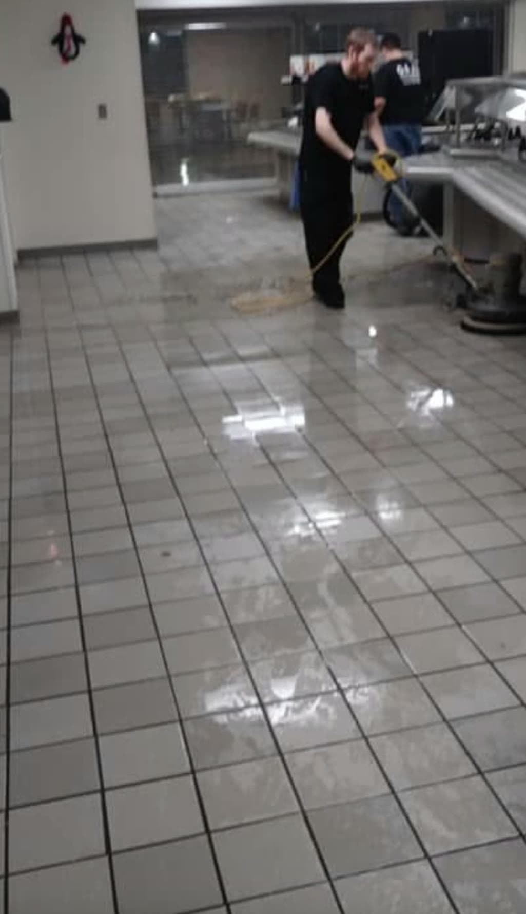A G & J's technician washing down a cafeteria kitchen floor beside the serving line.
