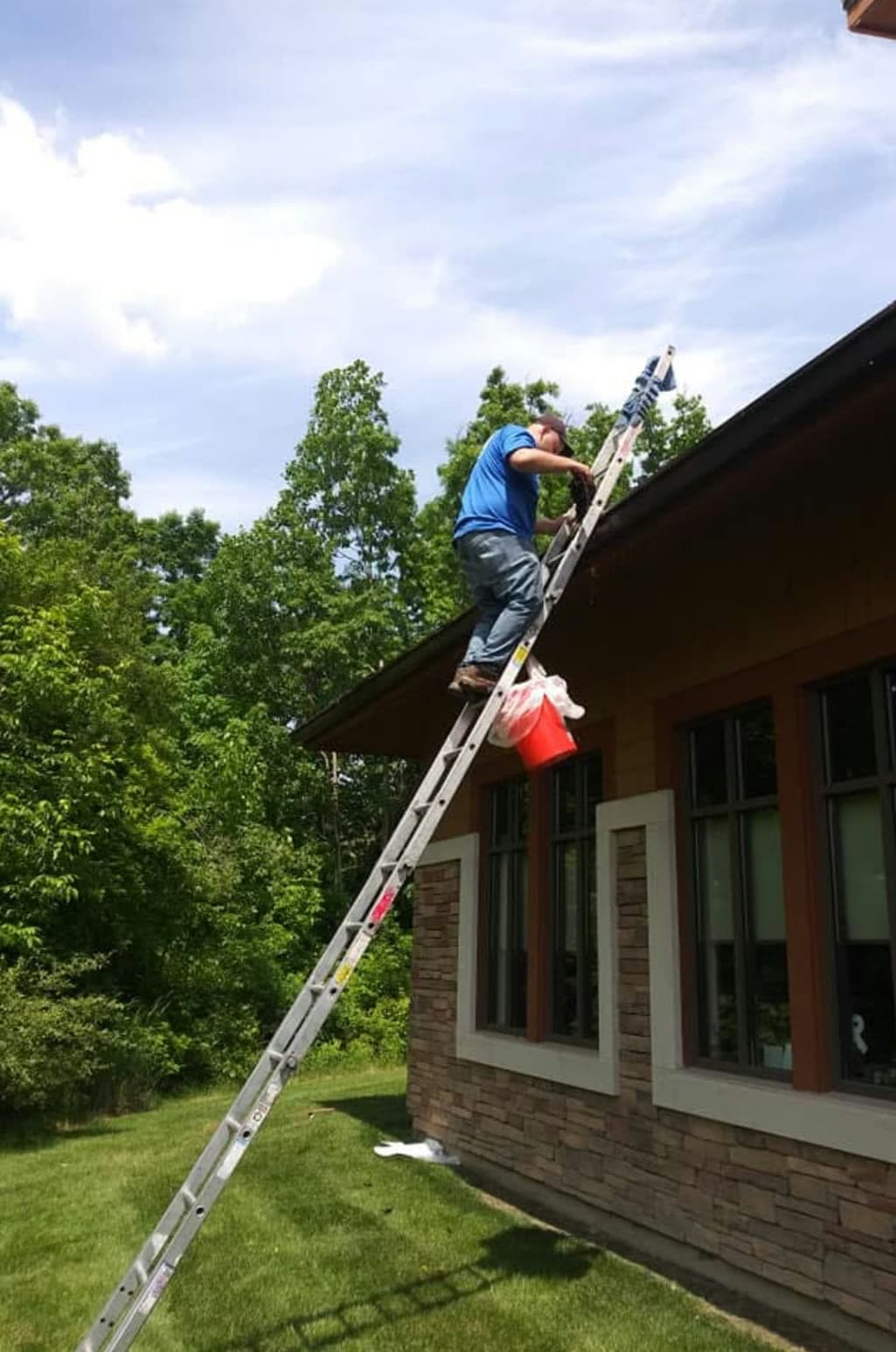 A G & J's technician on a ladder clearing a gutter on a residential property.