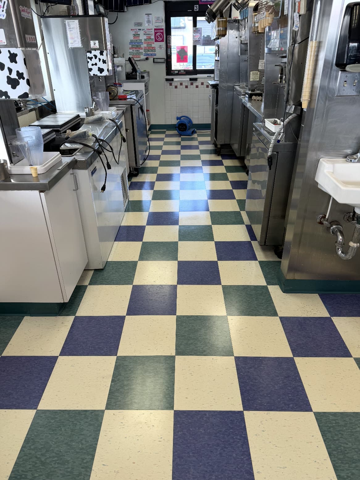 A food service kitchen with checkerboard tile floor freshly washed down and an air mover drying it.