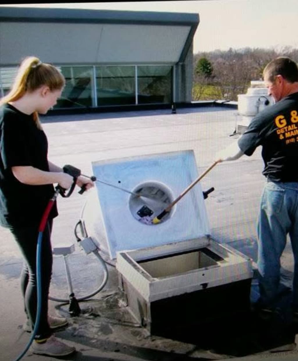 Two G & J's crew members pressure washing a rooftop kitchen exhaust unit.